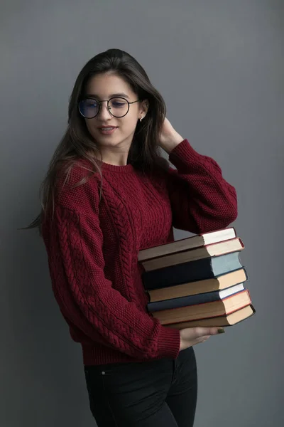 彼女の手に本を保持灰色の背景に ポーズを流れる髪を持つ少女のクローズアップ バーガンディのセーターとメガネを着て ロイヤリティフリーのストック写真