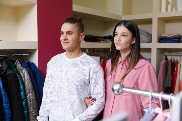 Smiling couple looking at new clothes.The young couple considers clothes in shop.Young nice couple in shop with purchases