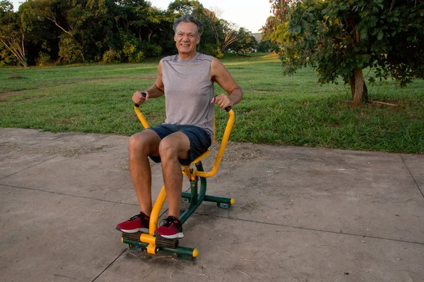 Fit Middle Aged Mature Man Working Out at an Outdoor Fitness Park using a Rowing Machine