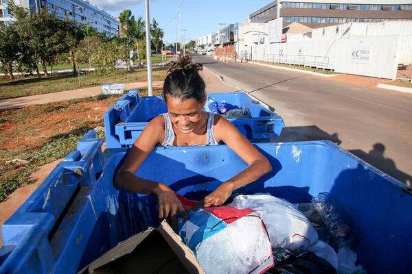 Brasilia, D.F., Brazil- June 11, 2019: A poor young mother digging through the Trash in an affluent neighborhood in the capital city of Brasilia, to try and earn some money to feed her kids. 