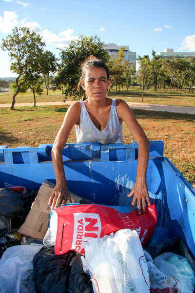 Brasilia, D.F., Brazil- June 11, 2019: A poor young mother digging through the Trash in an affluent neighborhood in the capital city of Brasilia, to try and earn some money to feed her kids. 