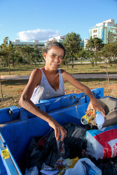 Brasilia, D.F., Brazil- June 11, 2019: A poor young mother digging through the Trash in an affluent neighborhood in the capital city of Brasilia, to try and earn some money to feed her kids. 