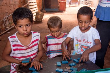 Planaltina, Goias, Brezilya-28 Nisan 2018: Brasilia'nın başkenti yakınlarındaki yoksul Planaltina bölgesinde evlerinin önünde domino oynayan üç kardeş 