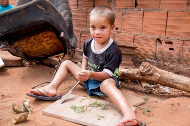 Planaltina, Gois, Brezilya-4 Ağustos 2018: Planaltina'nın fakir topluluğundan küçük bir çocuk arka bahçesinde kırık bir bıçakla oynuyor.  