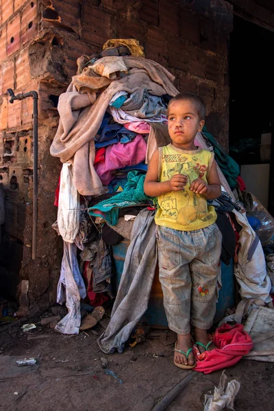 stock image Planaltina, Gois, Brazil-July 7, 2018: A little boy from the poor community of Planaltina standing outside his home in front of a big pile of laundry
