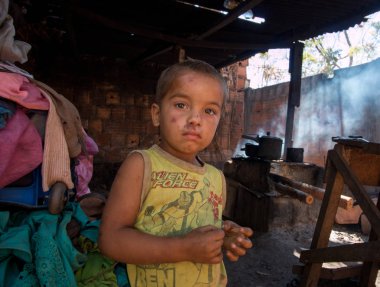 Planaltina, Gois, Brezilya-7 Temmuz 2018: Evinin önünde eğreti bir ateşle arka planda yemek pişiren zavallı bir çocuk.
