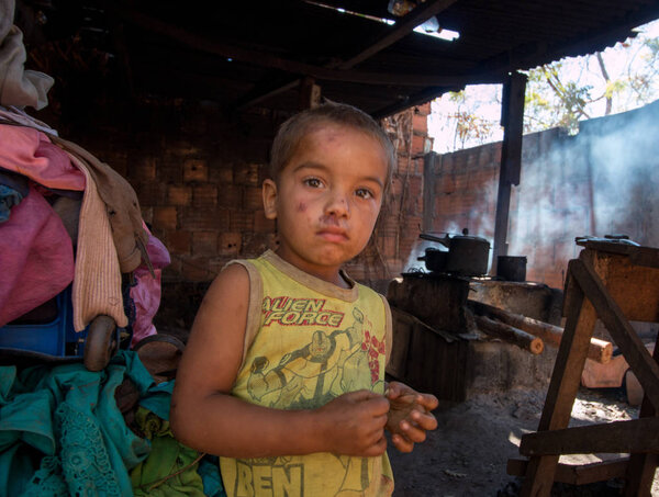 Planaltina, Gois, Brazil-July 7, 2018: A poor boy standing outside his home with a makeshift fire cooking food in the background.