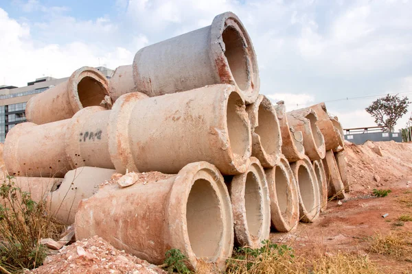 Sewage pipes piled up and stacked on the side of a dirt road