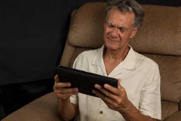 Olgun Centilmen Basit bir sandalyede oturmuş Akıllı Tabletine bakıyor.