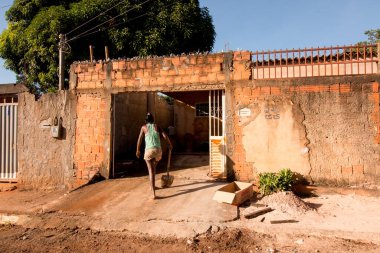 Planaltina, Goias, Brezilya-30 Mayıs 2020: Elinde kürek tutan bir kadın sokaktaki enkazı temizledikten sonra evine geri dönüyor.