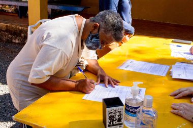 Planaltina, Goias, Brezilya-13 Haziran 2020: Koruyucu maske takan bir kadın, şehirdeki bir beslenme merkezinden bağış almak için bazı kağıt işleri imzalıyor