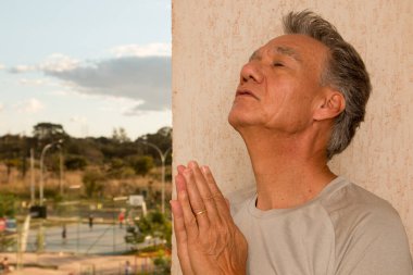 Balkonunda elleri bağlı dua eden bir adam var.