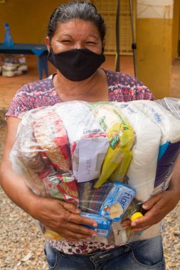 Planaltina, Goias, Brazil-May 16th 2020: A local feeding Center in Planaltina, hands out food and clothing to the poor people of the community while everyone wear their protective surgical mask. clipart