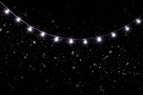 Christmas Lights, Garland in Snowfall with Small  Led Lamps Shining on Black Background.