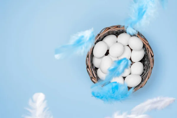 Hasır Sepette Beyaz Yumurtalar ve Dökümlü Kağıt Arkaplanda Tüyler. Paskalya sembollerinden biri. Bazı Tüyler Özellikle Bulanık Odakta.