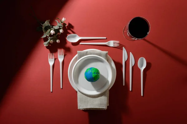 Dünya gezegeniyle servis masası, plastik tabaklar, kaşıklar, çatallar, bıçaklar, peçete, çiçekler ve petrol yağlı şarap kadehleri. Dünya Saati, Dünya Günü, Okyanus Günü ve diğer ECO tarihleri için ekoloji kavramı.