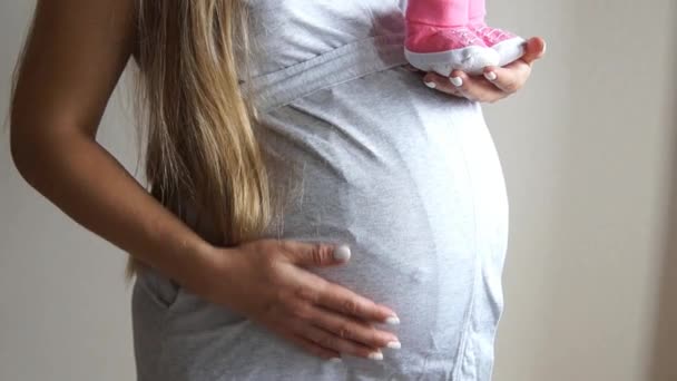 Femme enceinte tenant des chaussons de bébé. Une fille enceinte. Femme touchant son ventre enceinte — Video