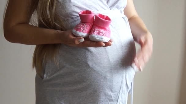 Femme enceinte tenant des chaussons de bébé. Une fille enceinte. Fille touchant ventre enceinte — Video