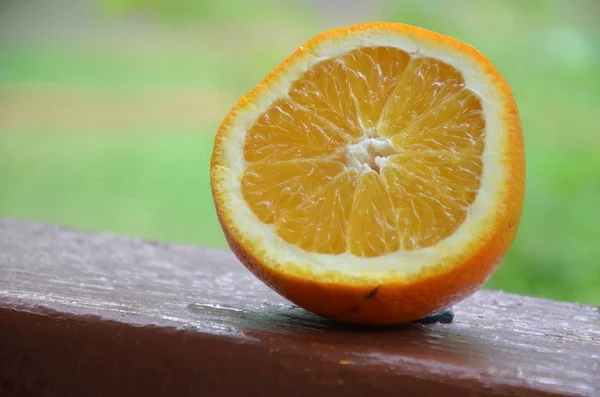 Orange, moitié orange, lobule orange et panier avec des oranges sur la table en bois sur le fond vert flou — Photo