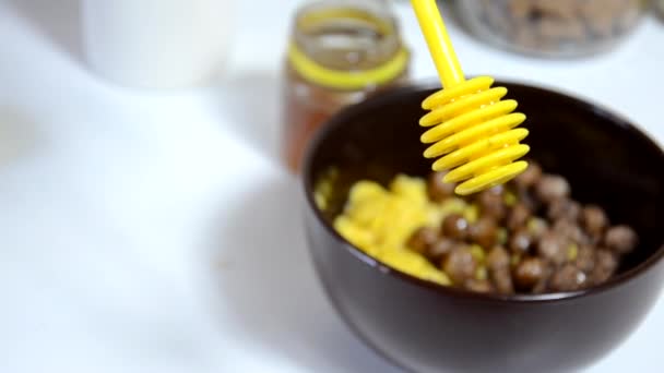 Vierta la miel al cereal del desayuno, bolas de chocolate en un tazón marrón. Desayuno saludable. Cuenco de dieta y cuchara con copos de maíz aislados sobre fondo blanco — Vídeos de Stock