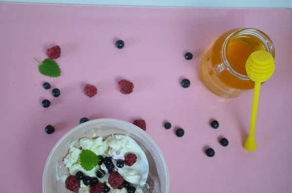里科塔新鲜的浆果和蜂蜜在粉红的桌子上。套餐奶酪、凝乳奶酪或碗里放有浆果的玉米粥。夏季甜点、早餐或健康小吃。一罐蜂蜜蓝莓和覆盆子 — 图库照片