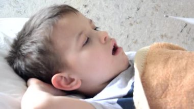 Ateşli bir geçmişi olan hasta bir çocukla kanepede yatıp dinlenen anne oğluna ilaç veriyor öksürük şurubu, boğaz spreyi, burnuna damla damlatıyor ve termometre koyuyor.