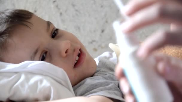 Baby-Medizin mit krankem Jungen auf Sofa liegend mit Fieber-Hintergrund, zu Hause liegend Mutter gibt ihrem Sohn Medikamente, Hustensaft, Halsspray, tropft in die Nase, legt ein Thermometer — Stockvideo