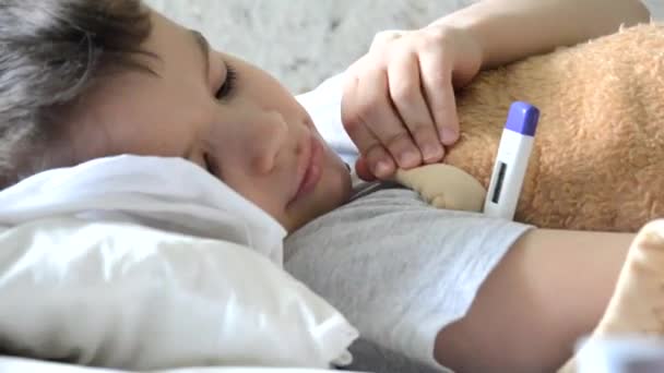 Medicamentos para bebés con niño enfermo acostado en un sofá con un fondo de fiebre, descansando en casa, mamá le da medicamentos a su hijo, jarabe para la tos, aerosol para la garganta, gotea en la nariz, le pone un termómetro — Vídeo de stock