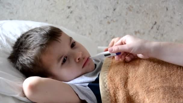 Baby geneeskunde met ziek kind jongen liggend op de bank met koorts achtergrond, rust thuis moeder geeft medicijnen aan haar zoon, hoestsiroop, keel spray, druipt in haar neus, zet een thermometer — Stockvideo