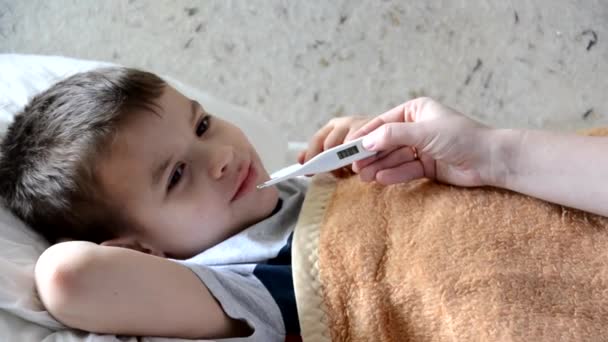 Baby geneeskunde met ziek kind jongen liggend op de bank met koorts achtergrond, rust thuis moeder geeft medicijnen aan haar zoon, hoestsiroop, keel spray, druipt in haar neus, zet een thermometer — Stockvideo