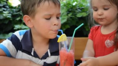 İki pipetle içen gülümseyen bir kız ve erkek. Erkek ve kız dışarıda oturmuş smoothie içiyorlar. Şirin erkek ve kız kardeşler ferahlatıcı bir kokteil ya da karpuz kokteyli içerler.