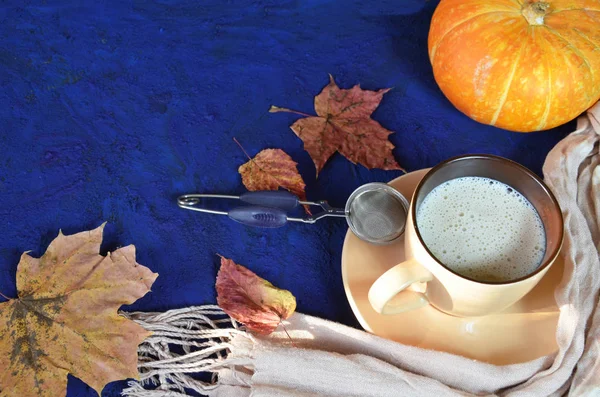 Pumpkin spiced latte or coffee in cup, dry leaves, gifts on dark blue table. Autumn or winter hot drink. Space for text, top view, copy space