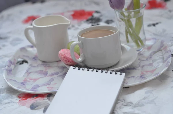 Bandeja con cuaderno de bocetos de papel, teléfono inteligente y flores de primavera sobre ropa de cama rosa. Relajarse, o trabajar, o escribir un diario o blog en la cama en casa . — Foto de Stock