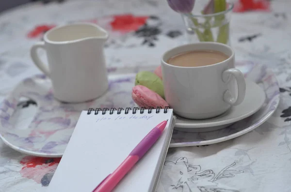 Bandeja con cuaderno de bocetos de papel, teléfono inteligente y flores de primavera sobre ropa de cama rosa. Relajarse, o trabajar, o escribir un diario o blog en la cama en casa . — Foto de Stock