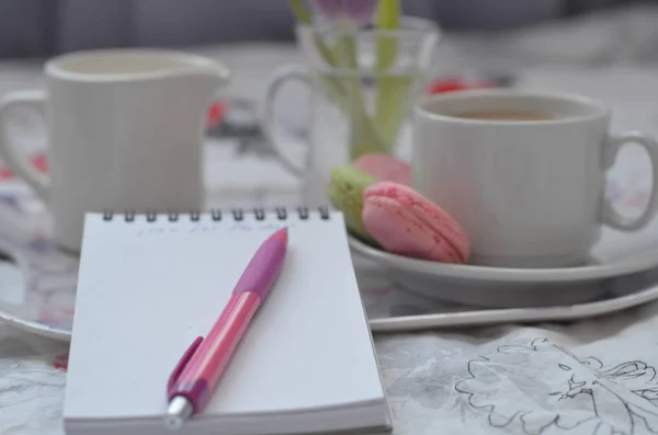 pembe yatak üzerinde kağıt sketchbook, akıllı telefon ve bahar çiçekleri ile tepsi. Evde rahatlatıcı, ya da çalışma, ya da evde yatakta günlük veya blog yazma.