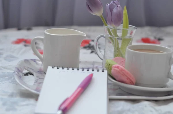 pembe yatak üzerinde kağıt sketchbook, akıllı telefon ve bahar çiçekleri ile tepsi. Evde rahatlatıcı, ya da çalışma, ya da evde yatakta günlük veya blog yazma.
