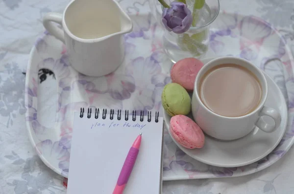 Bandeja con cuaderno de bocetos de papel, teléfono inteligente y flores de primavera sobre ropa de cama rosa. Relajarse, o trabajar, o escribir un diario o blog en la cama en casa . — Foto de Stock