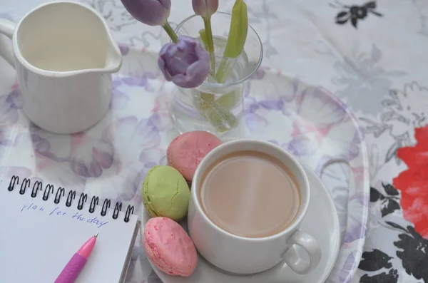 Bandeja con cuaderno de bocetos de papel, teléfono inteligente y flores de primavera sobre ropa de cama rosa. Relajarse, o trabajar, o escribir un diario o blog en la cama en casa . — Foto de Stock