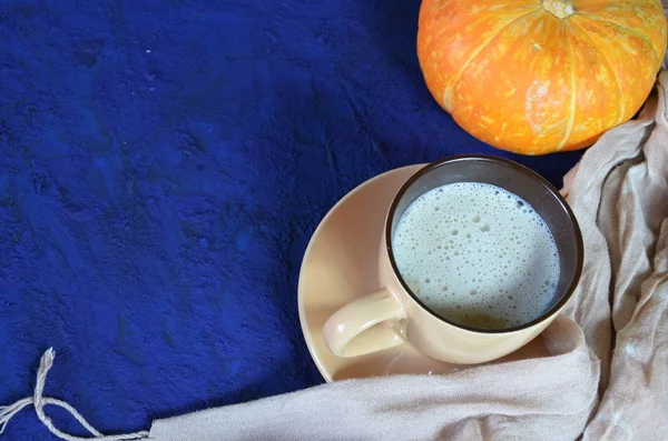 Pumpkin spiced latte or coffee in cup, dry leaves, gifts on dark blue table. Autumn or winter hot drink. Space for text, top view, copy space