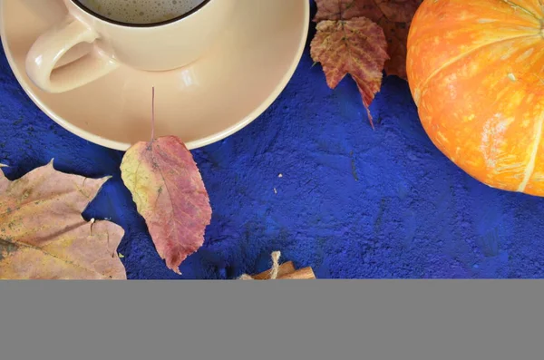 Pumpkin spiced latte or coffee in cup, dry leaves, gifts on dark blue table. Autumn or winter hot drink. Space for text, top view, copy space