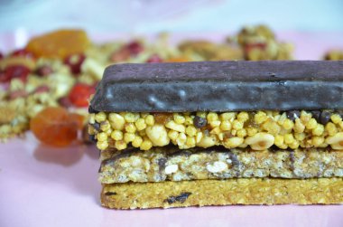 Granola barları, müsli barları veya yulaflı enerji barları, pembe arka planda hurma ve fındıklar, yakın plan. Yoga, fitness ve sporcular için aperatif, fitness barı, diyet konsepti.