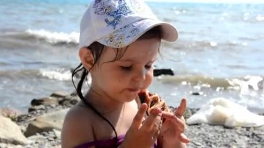 Mutlu kız sahilde meyveli tatlı turta ve fast food yiyor. Sağlıklı ve lezzetli atıştırmalıklar. Arka planda güzel deniz, tatiller, tatil, çocukluk