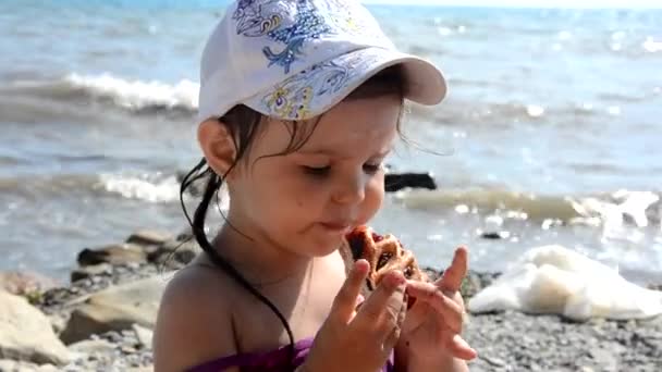 Щаслива дівчина їсть смачний солодкий пиріг з ягодами фаст-фуду на пляжі. Здоровий і смачний перекус. красиве море на фоні, свята, відпустка, дитинство — стокове відео