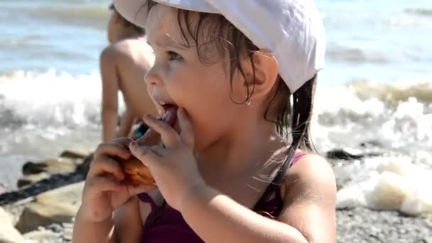 Menina feliz comer deliciosa torta doce com bagas fast food na praia. Lanche saudável e saboroso. belo mar no fundo, feriados, férias, infância — Vídeo de Stock