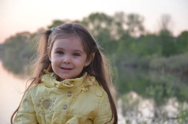 一个穿着秋天或春天夹克的小女孩站在湖边 微笑着 深蓝色底的小湖畔的游客 — 图库照片