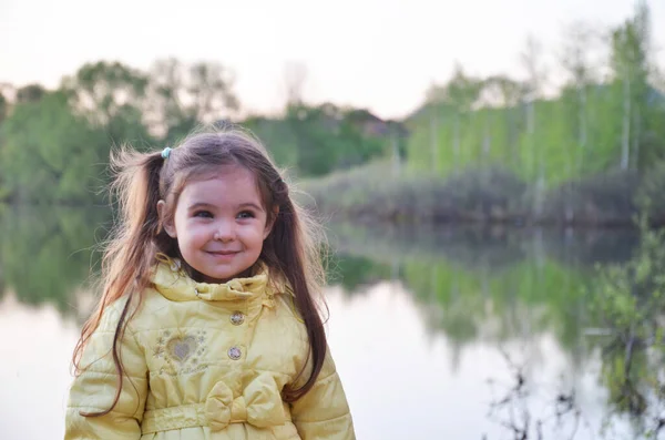 一个穿着秋天或春天夹克的小女孩站在湖边 微笑着 深蓝色底的小湖畔的游客 — 图库照片