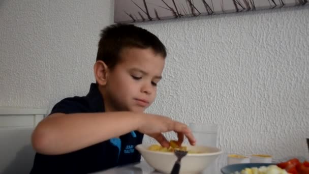 Leuke jongen eet lunch, ontbijt of diner thuis met een vork, drinkt water. Gezond eten thuis. Tegen de achtergrond van een witte muur. kinderen die gezond eten — Stockvideo