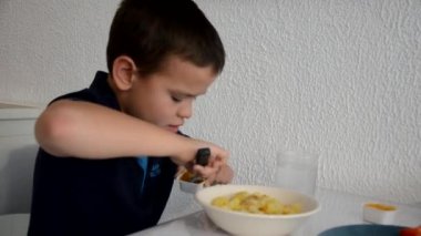 Tatlı çocuk öğle yemeği, kahvaltı ya da akşam yemeğini çatalla yer, su içer. Evde sağlıklı beslenme. Beyaz bir duvarın arkasında. Çocuklar sağlıklı besleniyor.