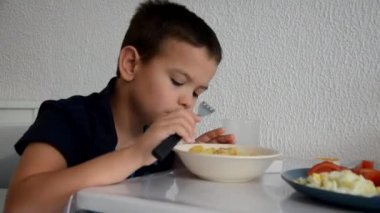 Tatlı çocuk öğle yemeği, kahvaltı ya da akşam yemeğini çatalla yer, su içer. Evde sağlıklı beslenme. Beyaz bir duvarın arkasında. Çocuklar sağlıklı besleniyor.