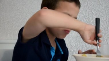 Tatlı çocuk öğle yemeği, kahvaltı ya da akşam yemeğini çatalla yer, su içer. Evde sağlıklı beslenme. Beyaz bir duvarın arkasında. Çocuklar sağlıklı besleniyor.